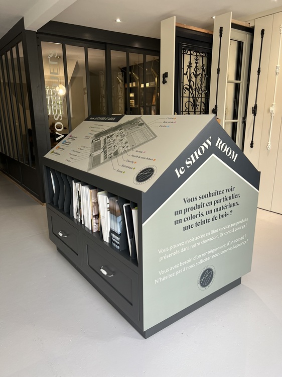 Un meuble pédagogique en clin d'œil à la maison, imaginé pour montrer, toucher et comprendre les différentes solutions de menuiserie disponibles. Support également d'une signalétique avec un visuel conçu pour montrer l’étendue des savoir-faire de l’Atelier